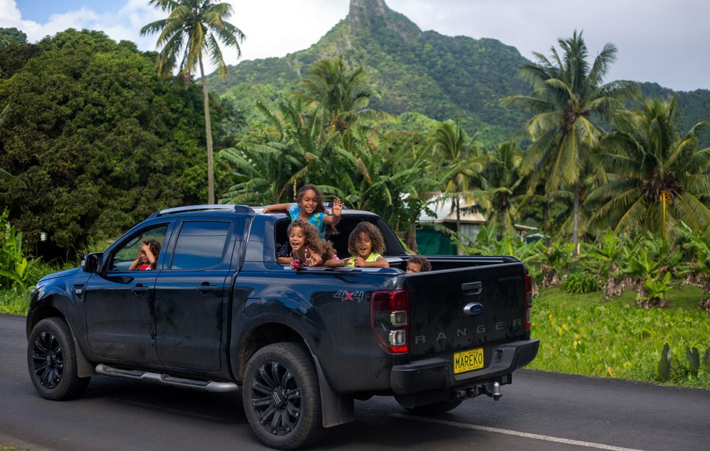 Children on the back of a ute with palm trees. 